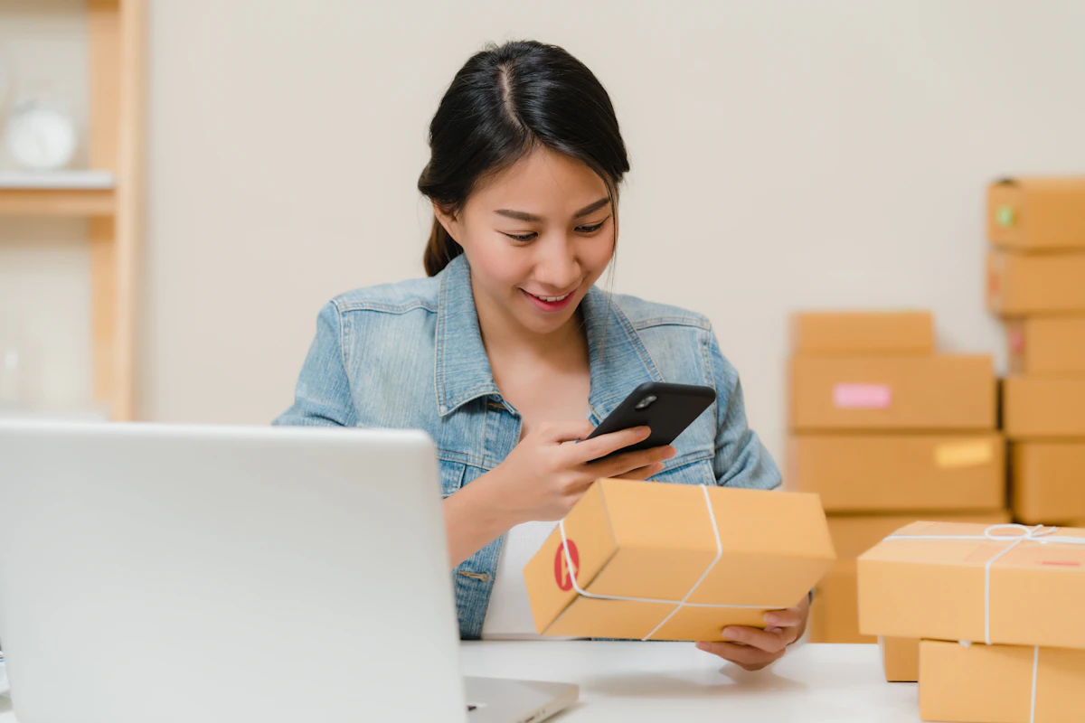 D2C seller packing ecommerce parcels while checking orders on a phone